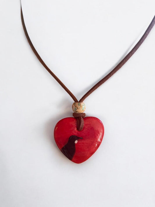Red heart-shaped pendant showing Tui Bird on a brown cord against a white background