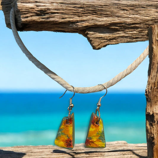 Colorful Sunflower earrings hanging on a wooden post with a beach background