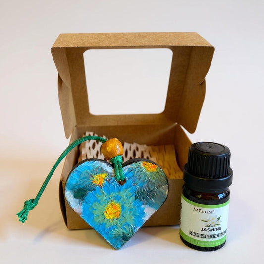 Heart-shaped painted terracotta essential oil difusser with a bottle of Jasmine essential oil in front of a cardboard gift box.