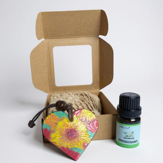 Open cardboard box with a colorful heart-shaped pendant and a bottle of essential oil on a white background