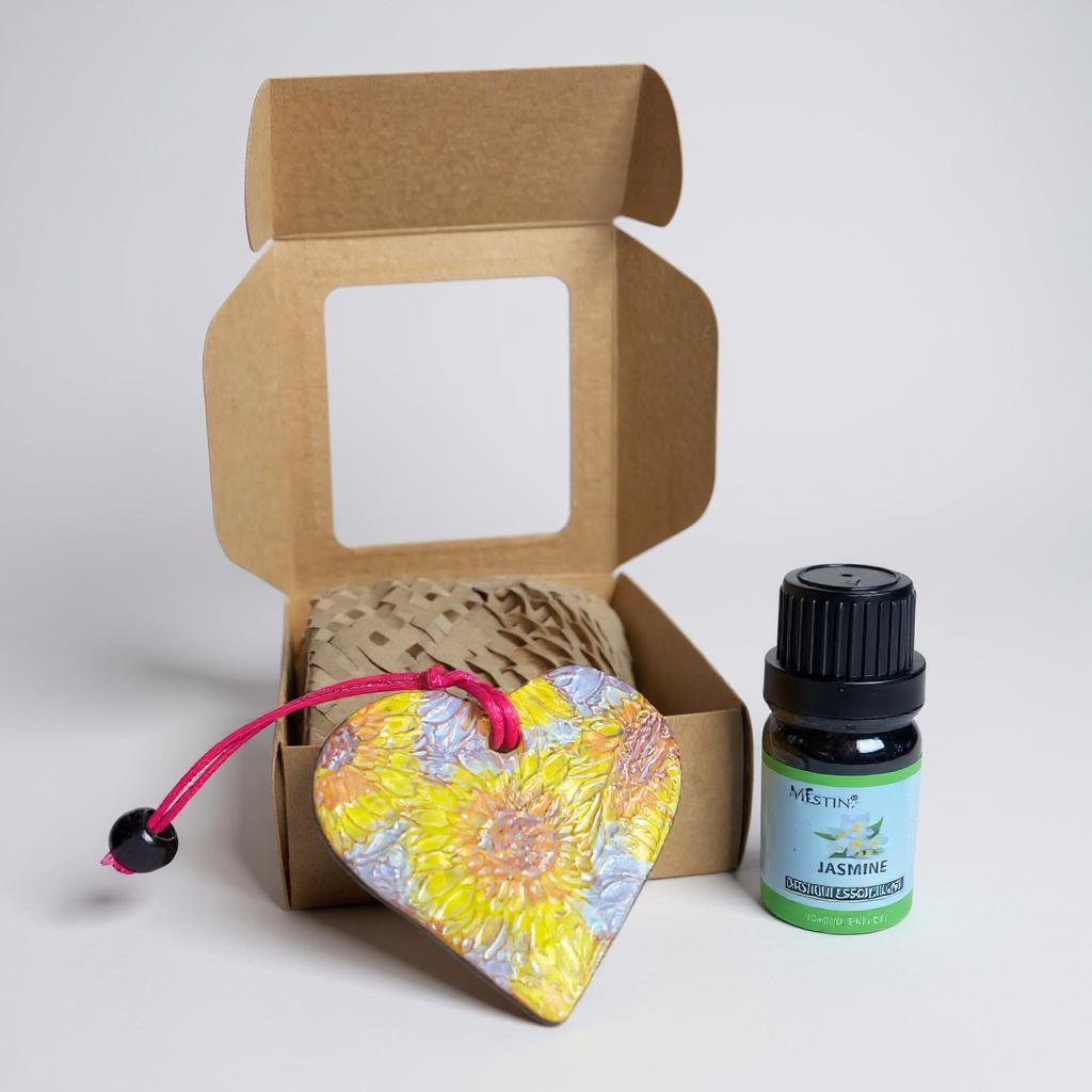 Heart-shaped floral pendant with pink string and a bottle of essential oil in front of an open cardboard box.