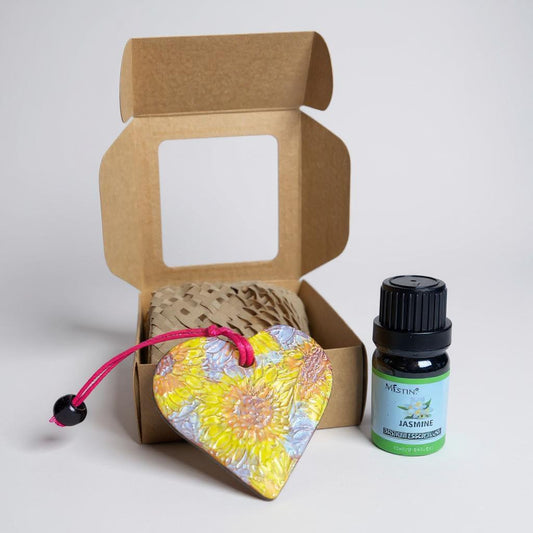 Heart-shaped floral pendant with pink string and a bottle of essential oil in front of an open cardboard box.