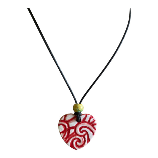 Heart-shaped pendant with red and white pattern on a black cord against a white background