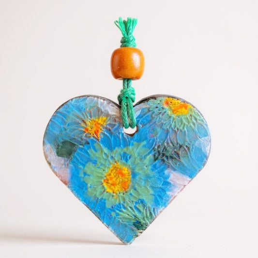 Heart-shaped terracotta essential oil diffuser with floral design and colorful bead on a white background