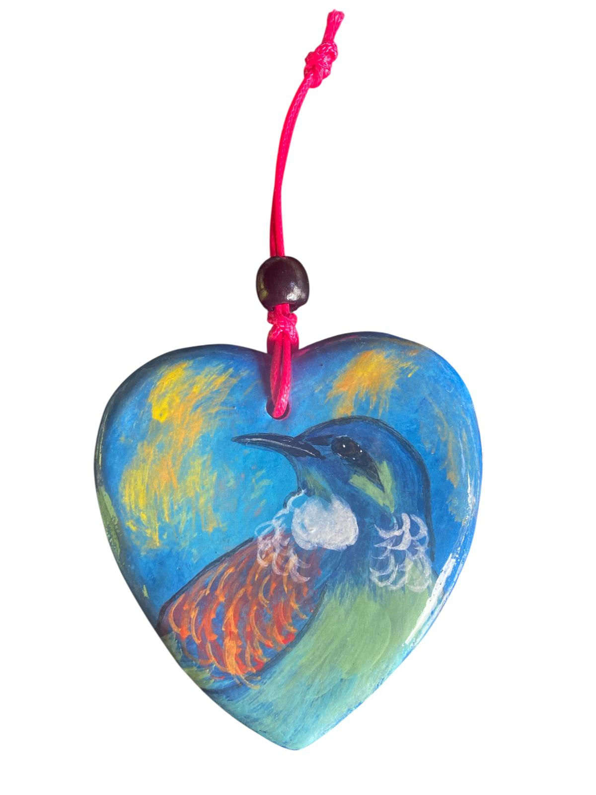 Heart-shaped ornament with a New Zealand native bird the Tui design on a pink string against a light gray background