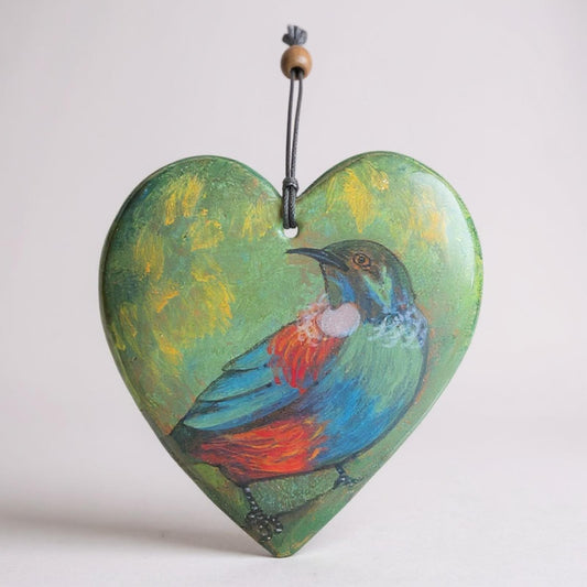 Heart-shaped ornament with a New Zealand native bird the Tui design on a black string against a light gray background