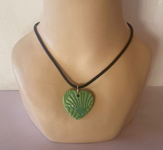 Green heart-shaped pendant on a black cord displayed on a mannequin neck.