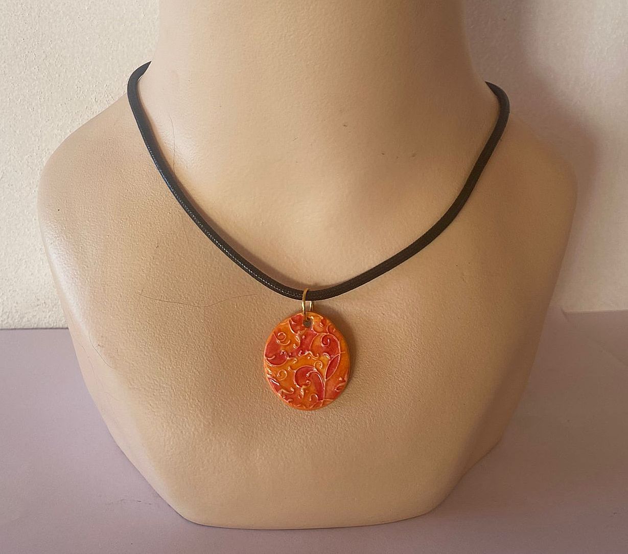 Necklace with a decorative orange pendant on a mannequin neck against a neutral background