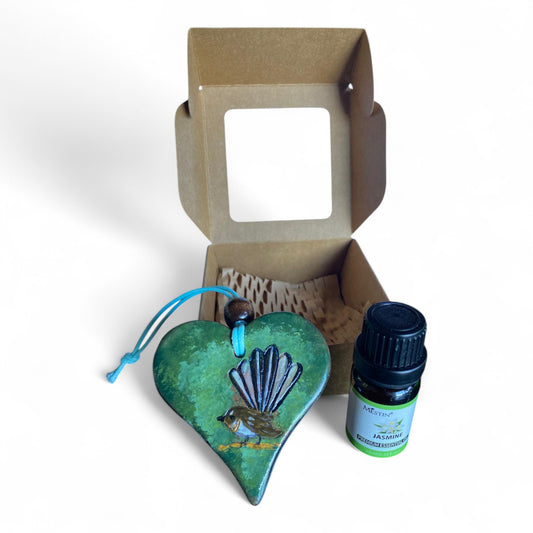Terracot heart shaped essential oil diffuser with fantail in front of giftbox with bottle of essential oil.