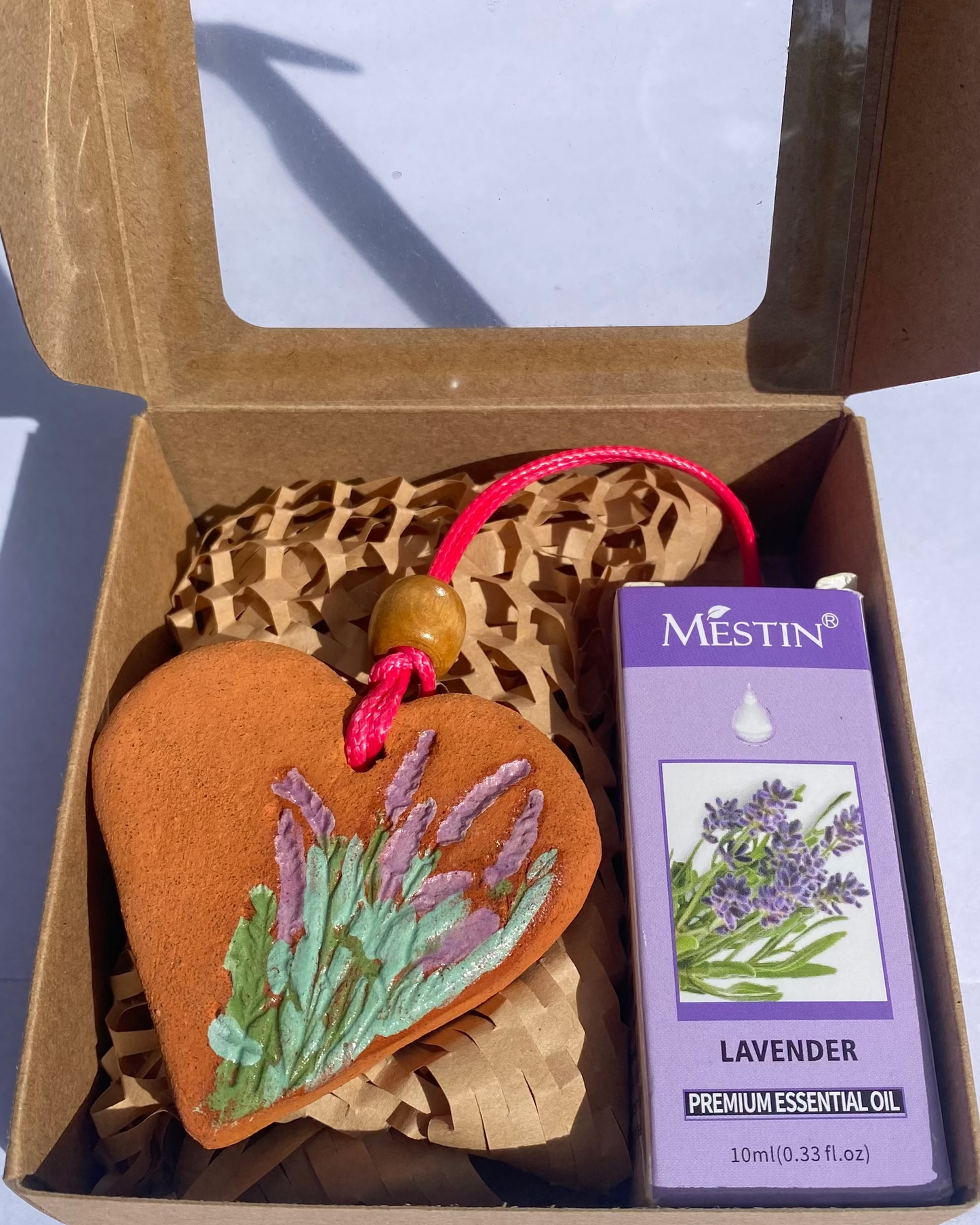 Heart-shaped lavender ornament and Mestin lavender essential oil packaging in an open cardboard box.