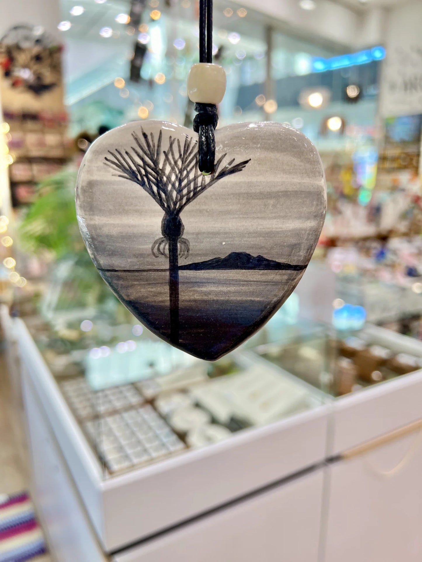 Heart-shaped pendant with New Zealand Nikau Palm design hanging in a store setting